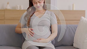 Happy Pregnant Woman sitting on sofa holding and stroking her big belly at home.Pregnancy of young woman enjoying with future life
