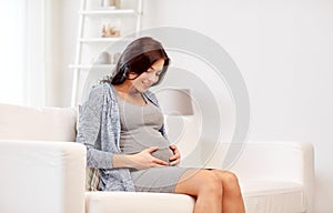 Happy pregnant woman sitting on sofa at home