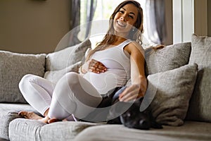 Happy pregnant woman sitting in sofa and pet her dog