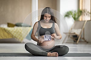 Happy Pregnant Woman Sitting On Yoga Mat And Holding Baby Sonography Scan