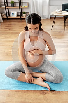 Happy pregnant woman sitting on yoga mat at home