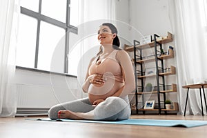 Happy pregnant woman sitting on yoga mat at home