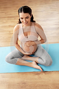 Happy pregnant woman sitting on yoga mat at home