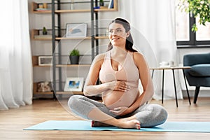 Happy pregnant woman sitting on yoga mat at home