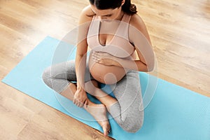 Happy pregnant woman sitting on yoga mat at home