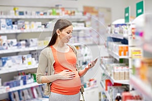 Happy pregnant woman with smartphone at pharmacy