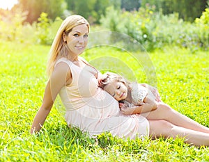 Happy pregnant woman, smiling mother and child lying on grass in summer