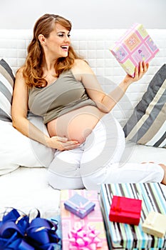 Happy pregnant woman on sofa with gifts for baby