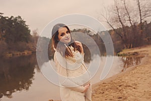 Happy pregnant woman in soft warm cozy outfit walking outdoors
