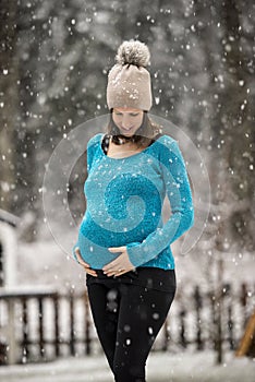 Happy pregnant woman standing outside in snowfall