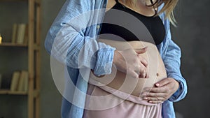 Happy pregnant woman stroking belly and playing with unborn baby, expectant mother in cozy room caring for pregnant