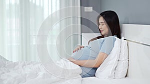 Happy pregnant woman stroking her belly on bed