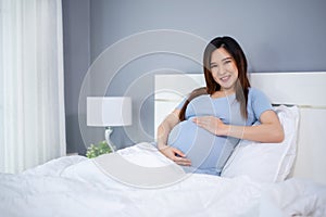 Happy pregnant woman stroking her belly on bed