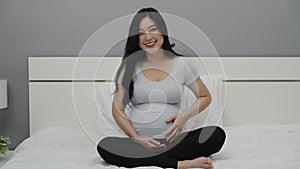 Happy pregnant woman stroking her belly on bed