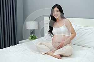 Happy pregnant woman stroking her belly on bed