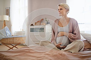 Happy pregnant woman stroking her belly, sitting on bed.