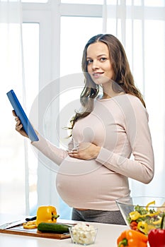 Happy pregnant woman with tablet pc cooking food