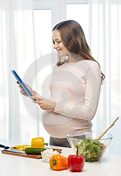 Happy pregnant woman with tablet pc cooking food