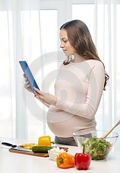 Happy pregnant woman with tablet pc cooking food