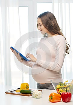 Happy pregnant woman with tablet pc cooking food