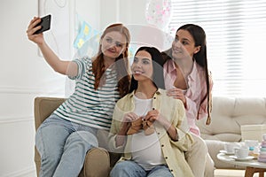 Happy pregnant woman taking selfie with friends at baby shower party