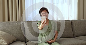 Happy pregnant woman talking via video conferencing app on smartphone