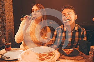 Happy pregnant woman with teenager boy eating pizza and enjoy it with savor. friends loves fast food. dinner in the