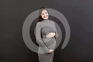 Happy pregnant woman touching her abdomen at Colored background. Future mother is wearing white underwear. Expecting of