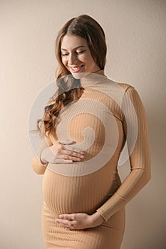 Happy pregnant woman touching her belly on beige background