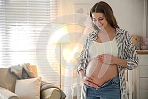 Happy pregnant woman touching her belly indoors