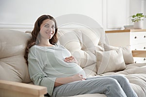 Happy pregnant woman touching her belly indoors