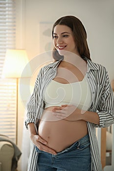 Happy pregnant woman touching her belly indoors