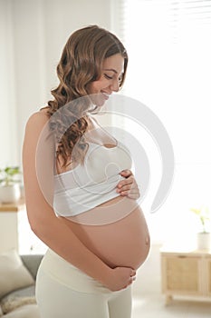 Happy pregnant woman touching her belly indoors