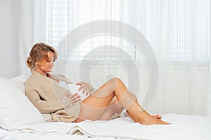 Happy pregnant woman touching her belly is sitting on bed