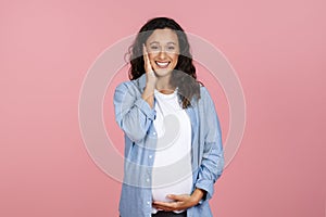 Happy pregnant woman touching her face and belly