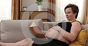 Happy pregnant woman touching her tummy at home. Pregnant woman resting on sofa, carresing her tummy