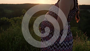 happy pregnant woman touching her tummy on top of mountain in tall grass before sunset. caring mother strokes large