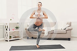 Happy pregnant woman training yoga in tree pose