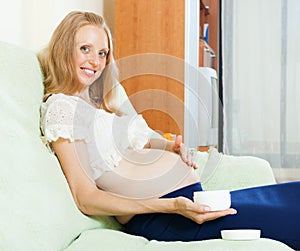 Happy pregnant woman using cosmetic cream