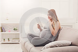 Happy pregnant woman using digital tablet.