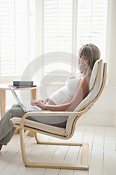 Happy Pregnant Woman Using Laptop On Chair