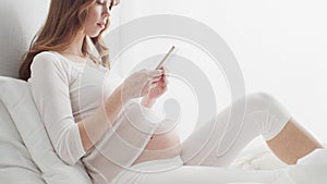 Happy pregnant woman using smartphone device. Pregnancy, motherhood, and expectation concept