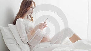 Happy pregnant woman using smartphone device. Pregnancy, motherhood, and expectation concept