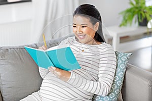 happy pregnant woman writing to diary at home