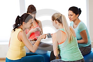 Happy pregnant women with gadgets in gym