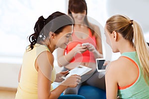 Happy pregnant women with gadgets in gym