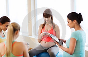 Happy pregnant women with gadgets in gym