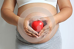 Happy pregnant women hand shows symbol heart shape with red hear