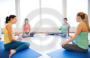 Happy pregnant women sitting on mats in gym