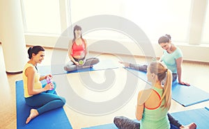 Happy pregnant women sitting on mats in gym